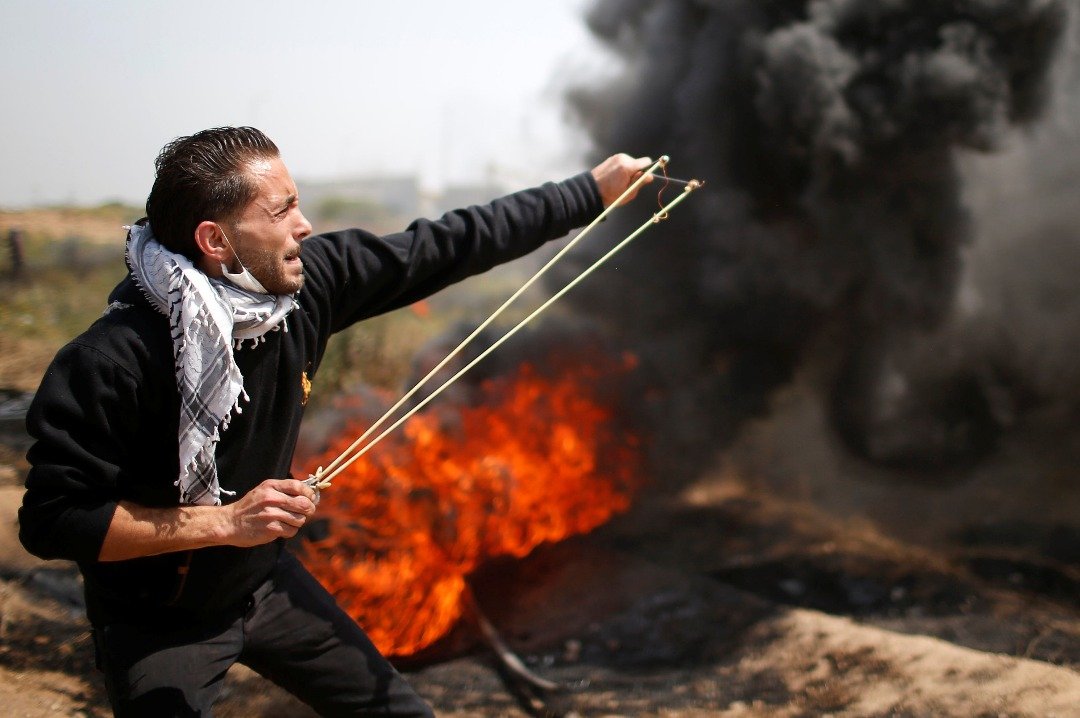 一名示威者在浓烟掩护下，用弹弓和石头射击以军。