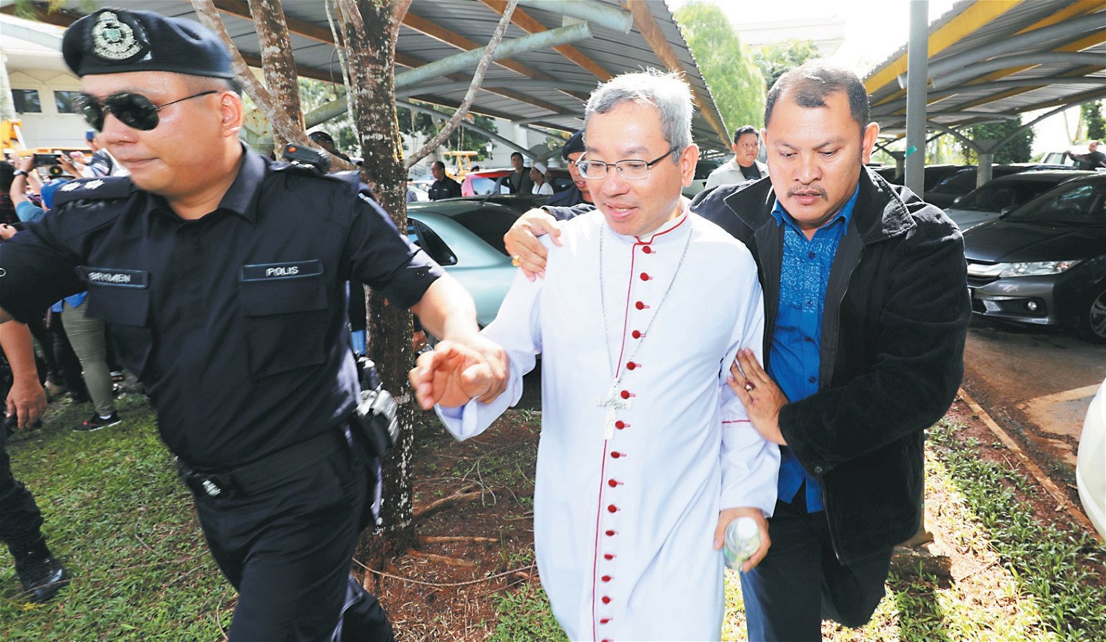 天主教古晋总教区主教傅云生（中）在警察和穆斯林领袖的协助下，离开现场。