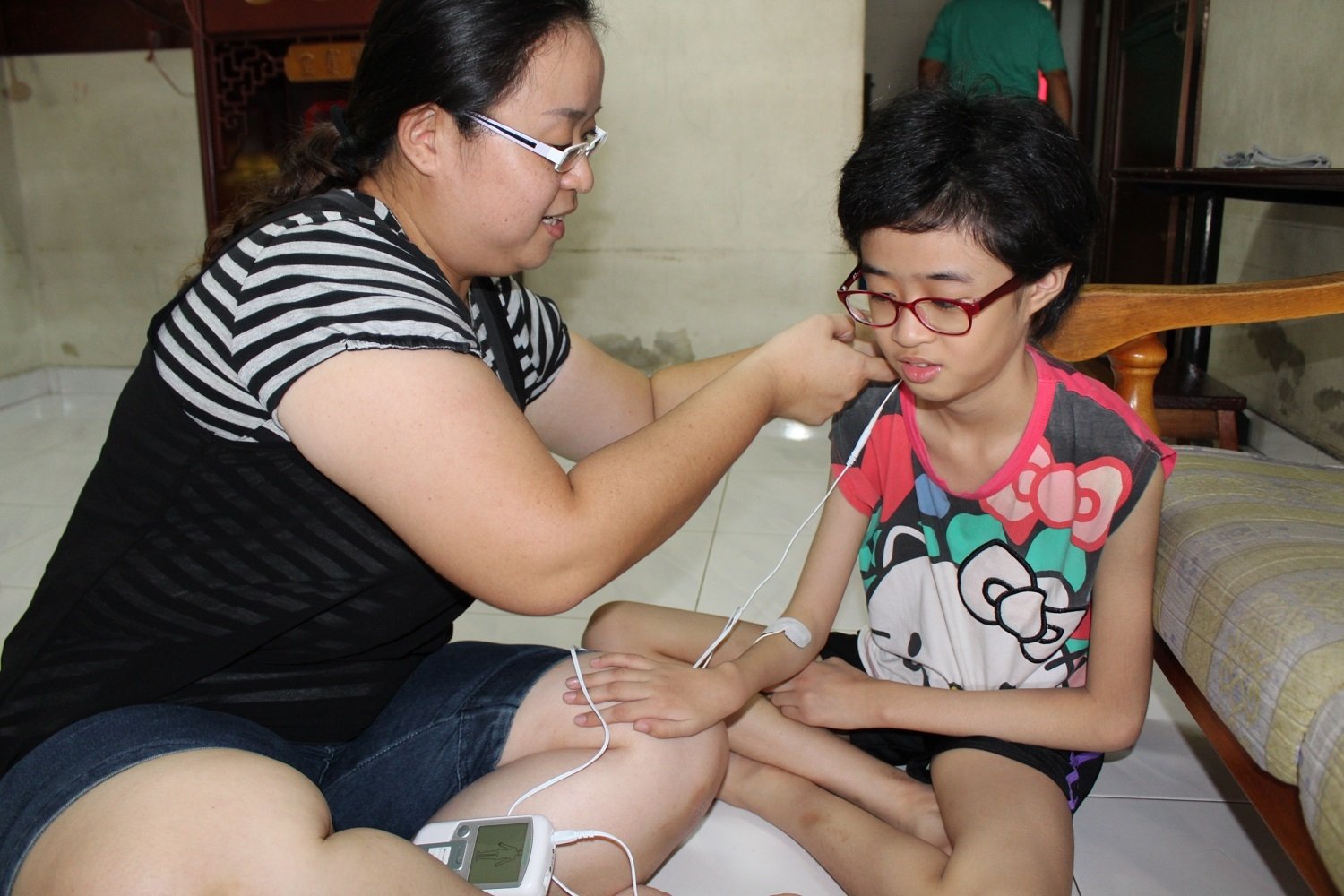 李彩铃（ 左）使用疼痛治疗装置， 为女儿进行超声治疗。
