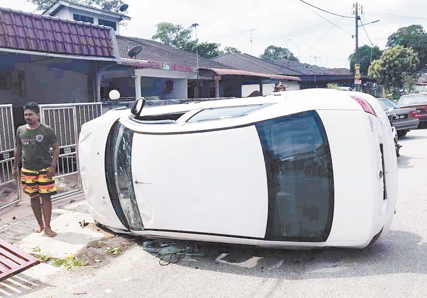 一辆白色轿车侧翻在路旁，轿车司机从车内爬出，没有受伤。