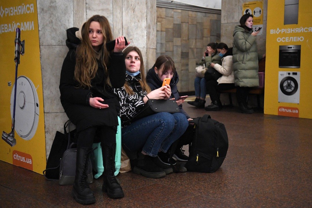 基辅民众带同行李到充作防空洞地铁站避难，许多人焦急地用手机查看最新消息。（图取自法新社）