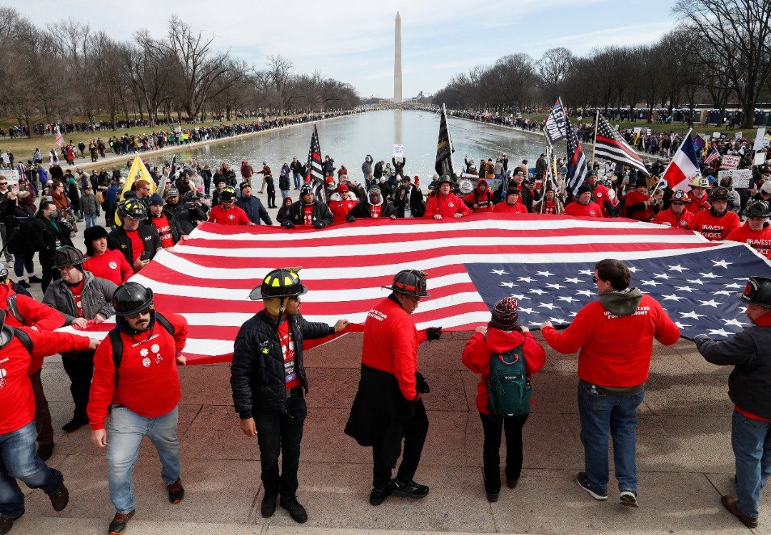 数千名美国人当地时间周日在华盛顿游行，反对他们所称新冠疫苗强制令的“暴政”，参与示威的消防员在华盛顿纪念碑展示大型美国国旗。（图取自路透社）