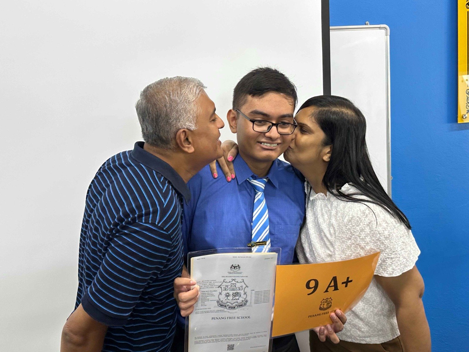 布文拉（中）在SPM考获9A+佳绩，其父亲嘉纳森（左起）及母亲苏米达向爱儿献吻。布文拉（左2）周四在父母及爷爷陪同下，前往母校槟城大英义中学，领取SPM成绩单。