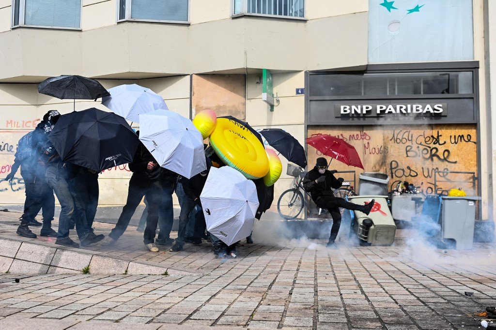 法国西部城市南特的示威者在周二的抗议活动上用雨伞为掩护，其中一人还用脚踢掉警方发射的催泪弹。（图取自法新社）
