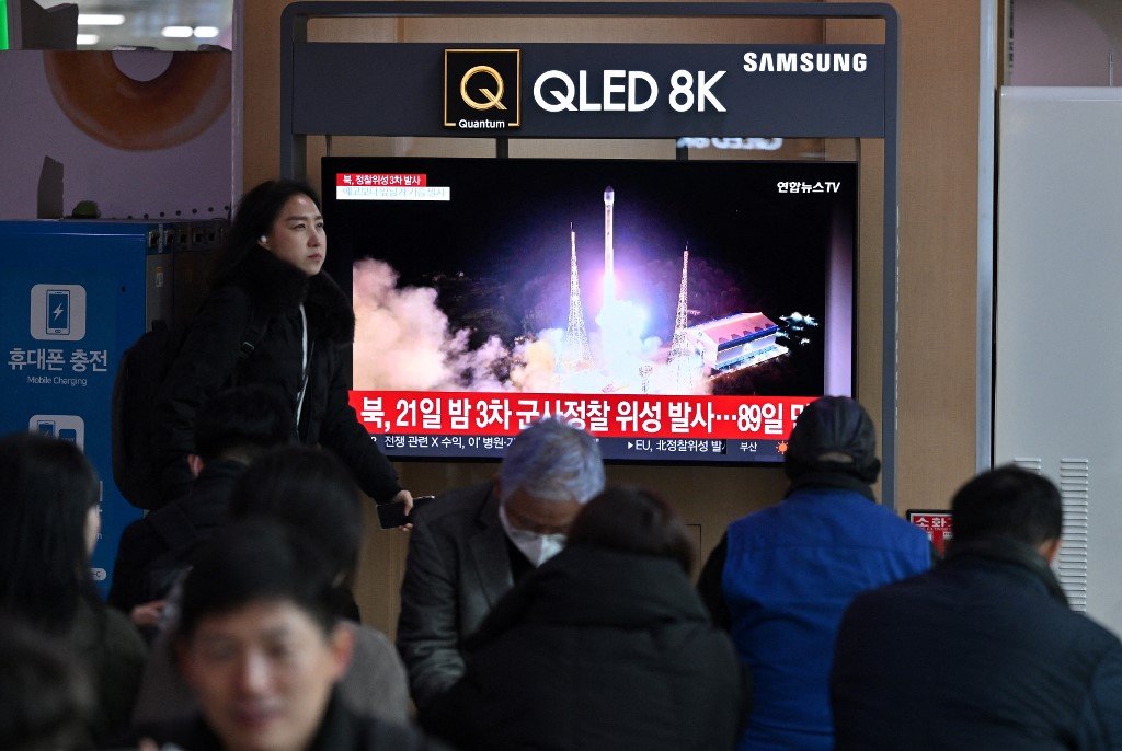 在韩国首尔一火车站，人们周三观看电视萤幕上播放的新闻画面，内容有关朝鲜在周二晚宣布成功试射侦察卫星。（图取自法新社）