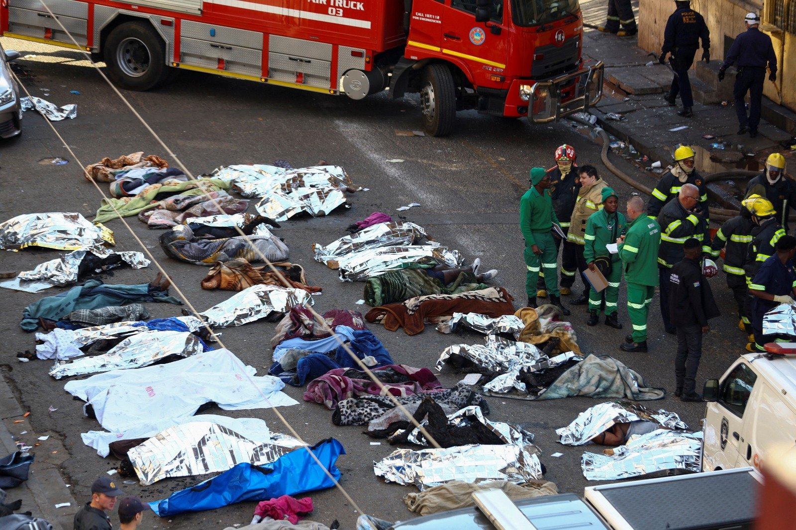 南非豪登省约翰内斯堡一栋5层建筑，当地时间周四发生致命火灾，救援人员和消防员将遇难者的遗体排列在现场空地上。（图取自路透社）