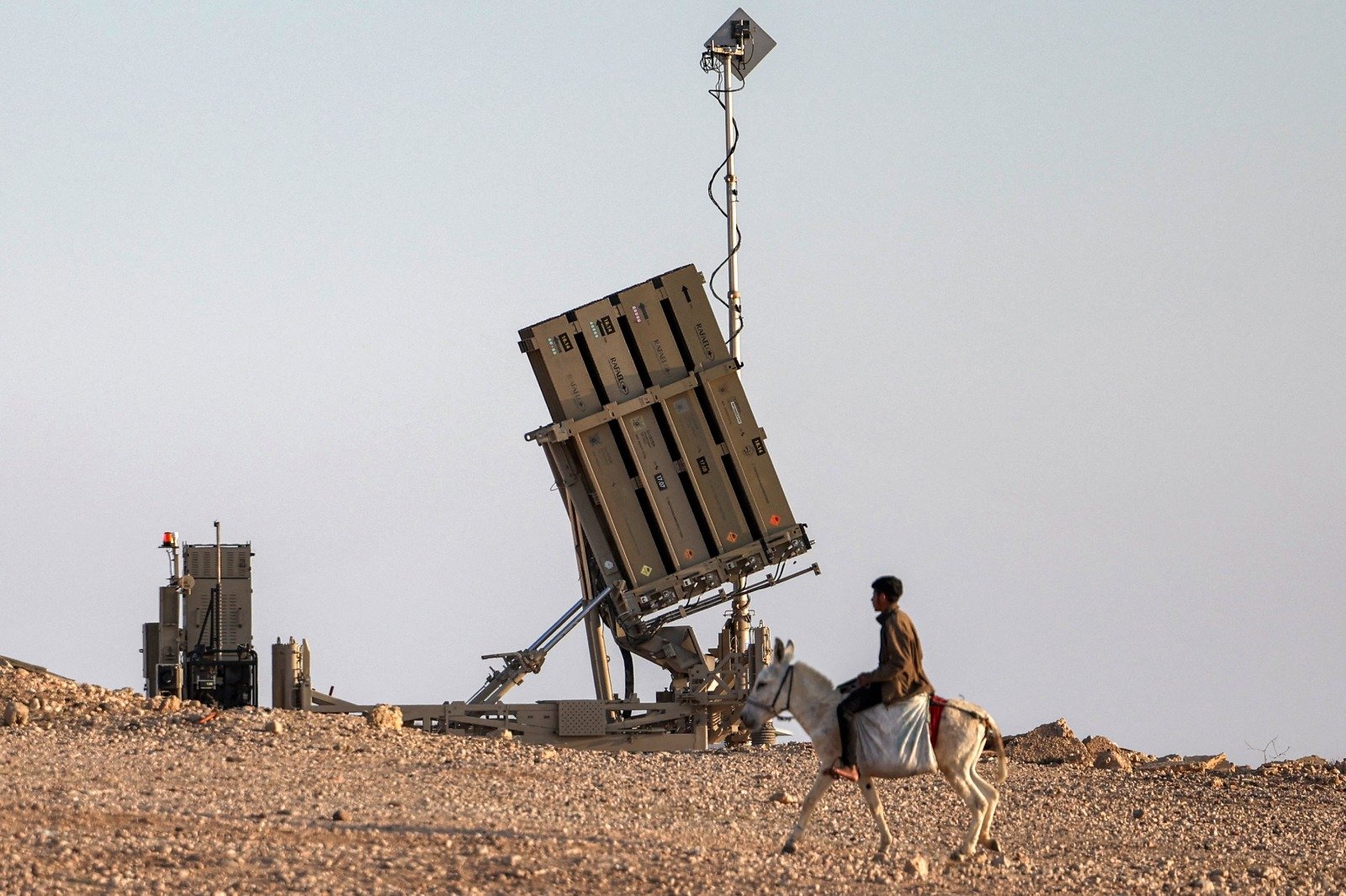 在内盖夫沙漠南部一个未被以色列当局承认的村庄，一名男孩周日骑著一头毛驴，靠近以色列“铁穹”导弹防御系统的一个炮台。（图取自法新社）