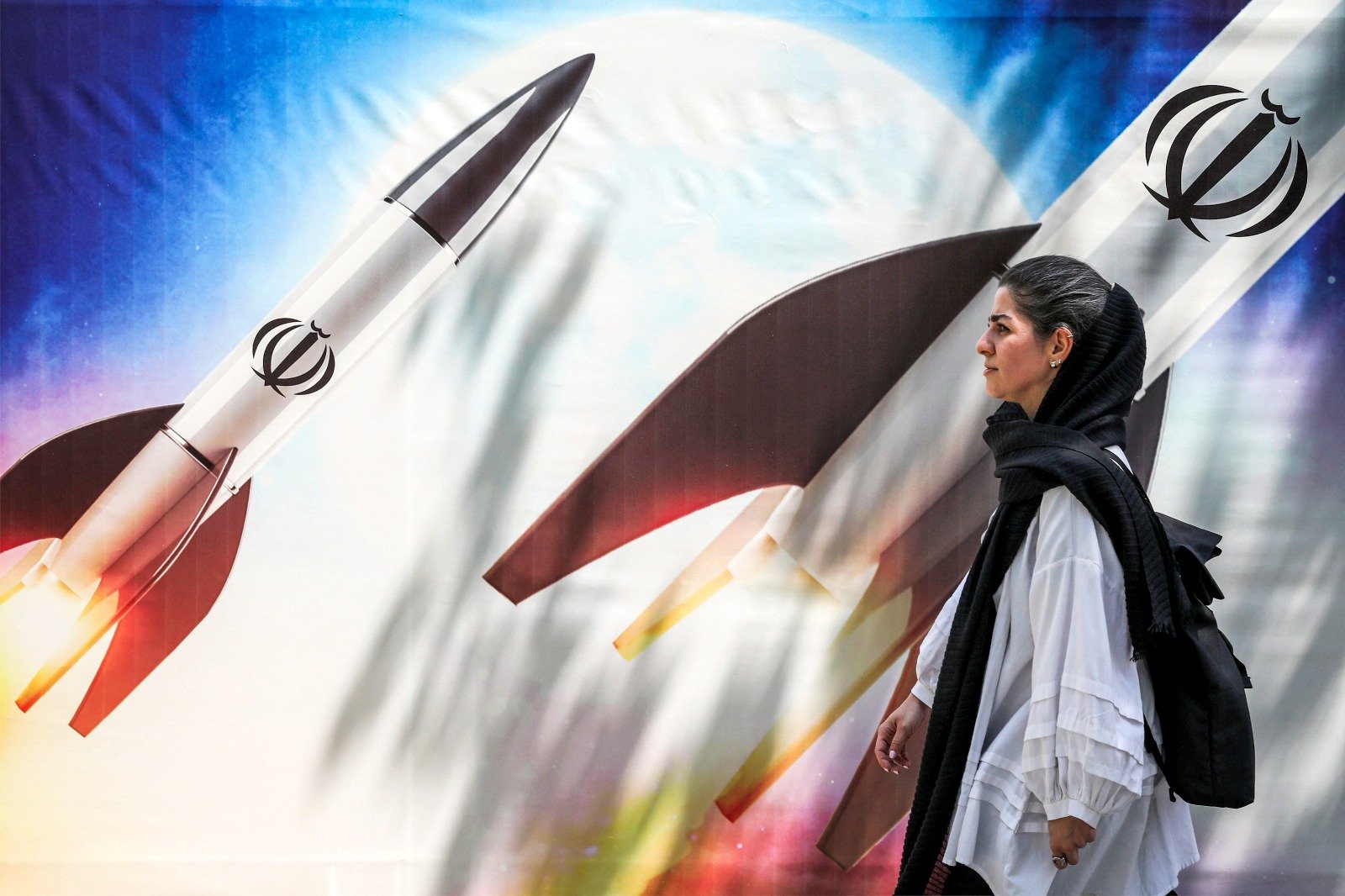 在伊朗首都德黑兰市中心，一名妇女周一走过一面横幅，上面画著正在发射带有伊朗伊斯兰共和国标志的导弹。（图取自法新社）