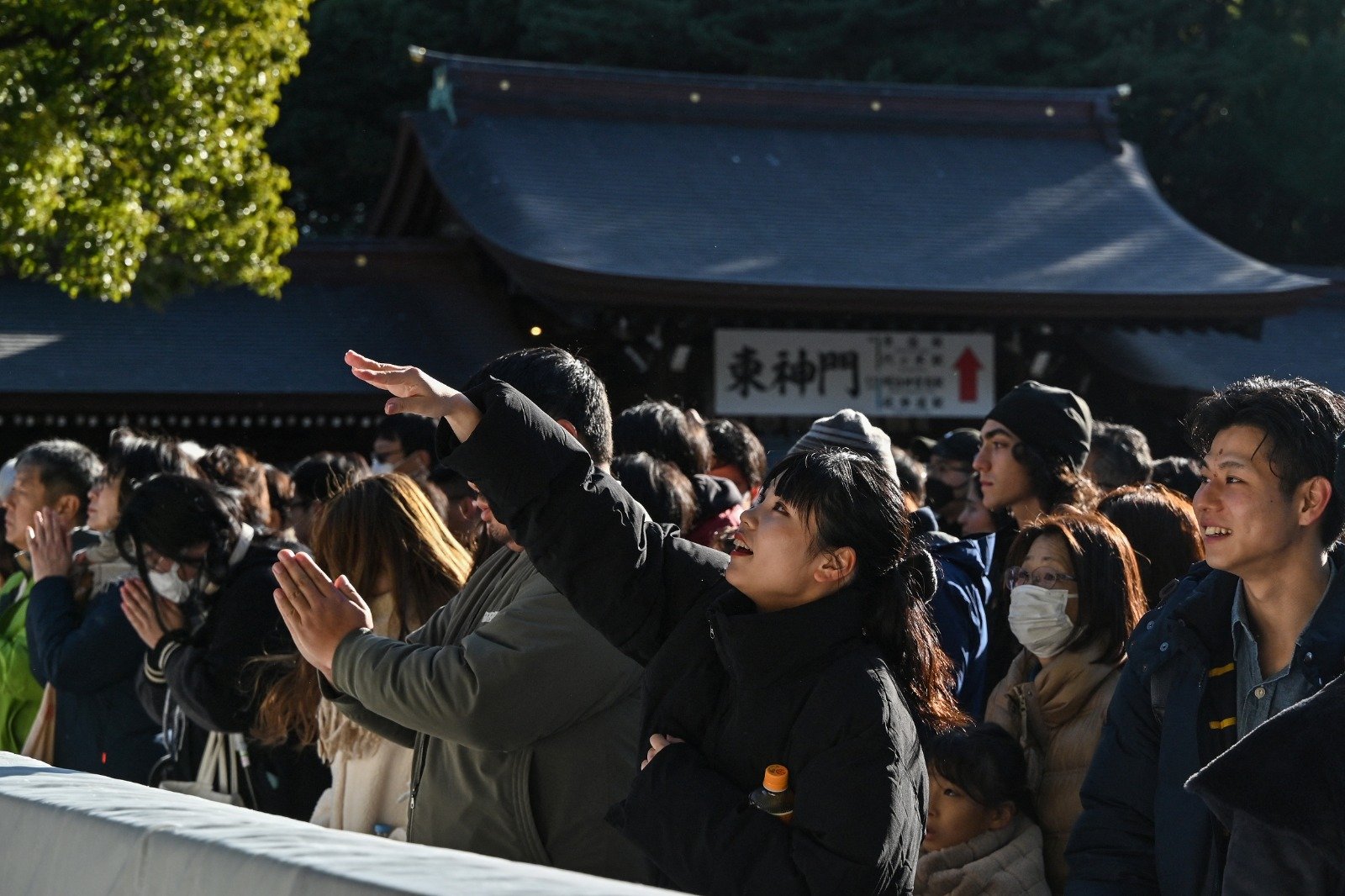 元旦第一天早上，一名年轻女子（中）在日本东京市中心的明治神宫投掷硬币祈福。（图取自法新社）