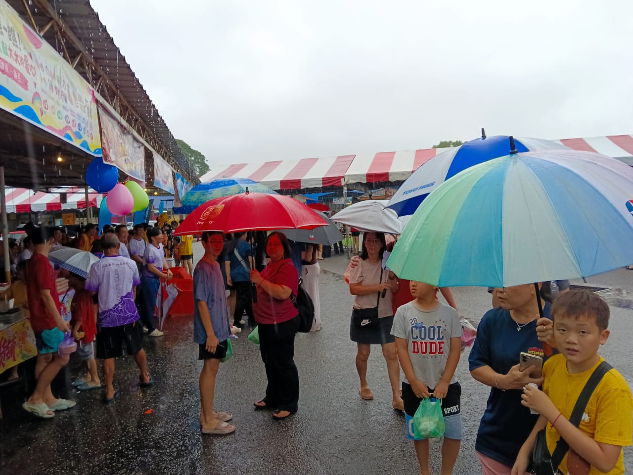 清晨一场长命雨来袭，校园地面湿漉，民众仍撑伞携老扶幼前来，义卖会在雨中热爆。