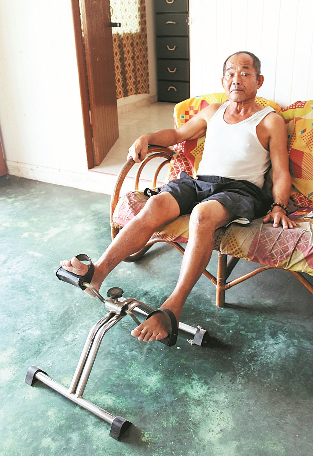 邓阿叻使用脚踏复健器，希望有朝一日能行动自如。