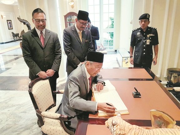 马哈迪（坐者）在吉打王宫访客签到簿上签名，左为前巫统峇都加湾区部副主席拿督凯鲁丁。