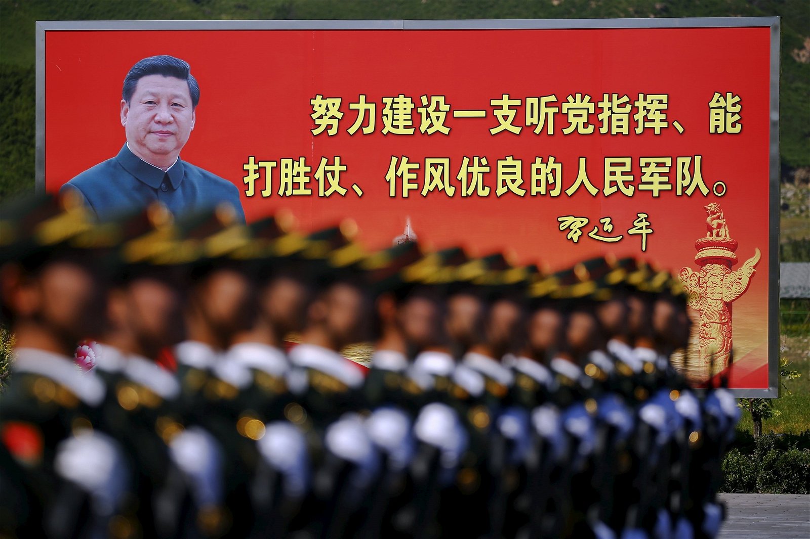 这是2015年中国人民抗日战争胜利70周年大阅兵前夕，在北京举行的阅兵排练，解放军阅兵队伍经过一个告示板，上面有中国国家主席习近平的肖像和标语。