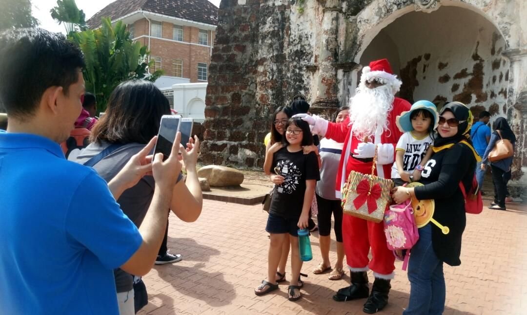 各族游客在甲州古城门前争相与圣诞老人合照，体现出我国不分种族和宗教，共同欢庆圣诞节的和谐一面。