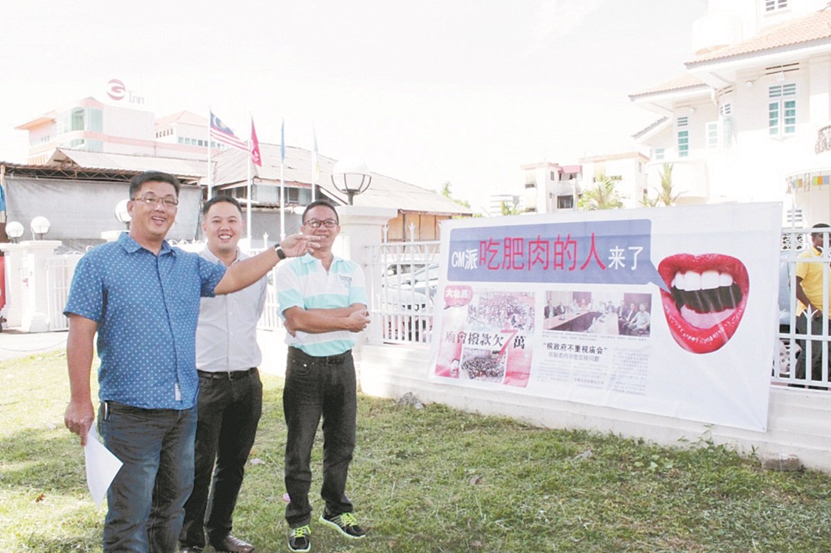 陈嘉亮（左）指著挂在槟民政党总部前的布条，暗讽即将到来的黄伟益。