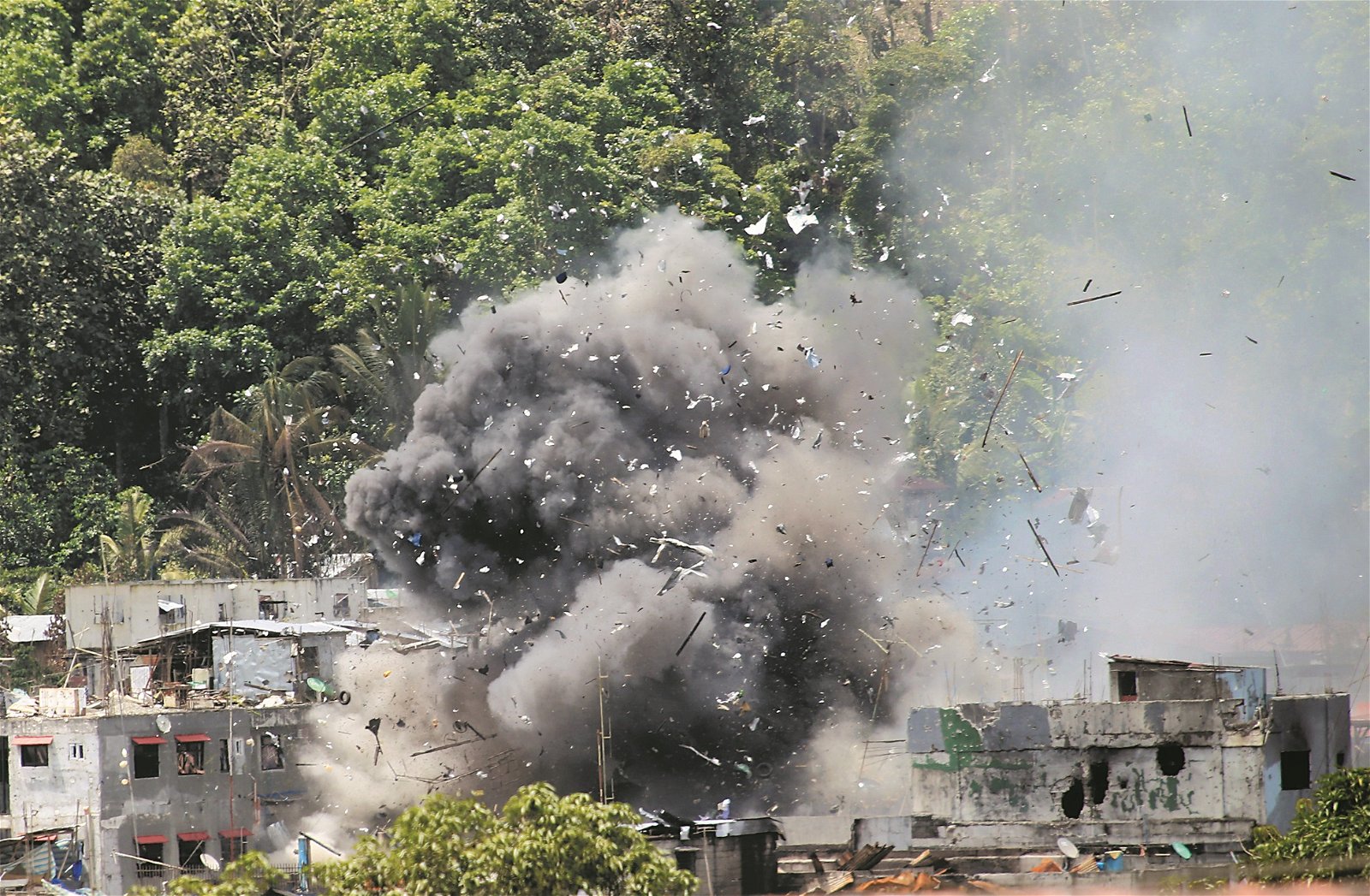 菲律宾政府军攻击型侦察机的导弹，击中地面的建筑，瓦砾和碎片被炸飞，现场冒出滚滚浓烟。