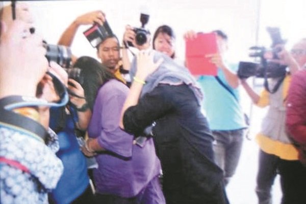 女被告（左2）避开媒体的镜头，用手掩住脸部，快速步入法庭内。