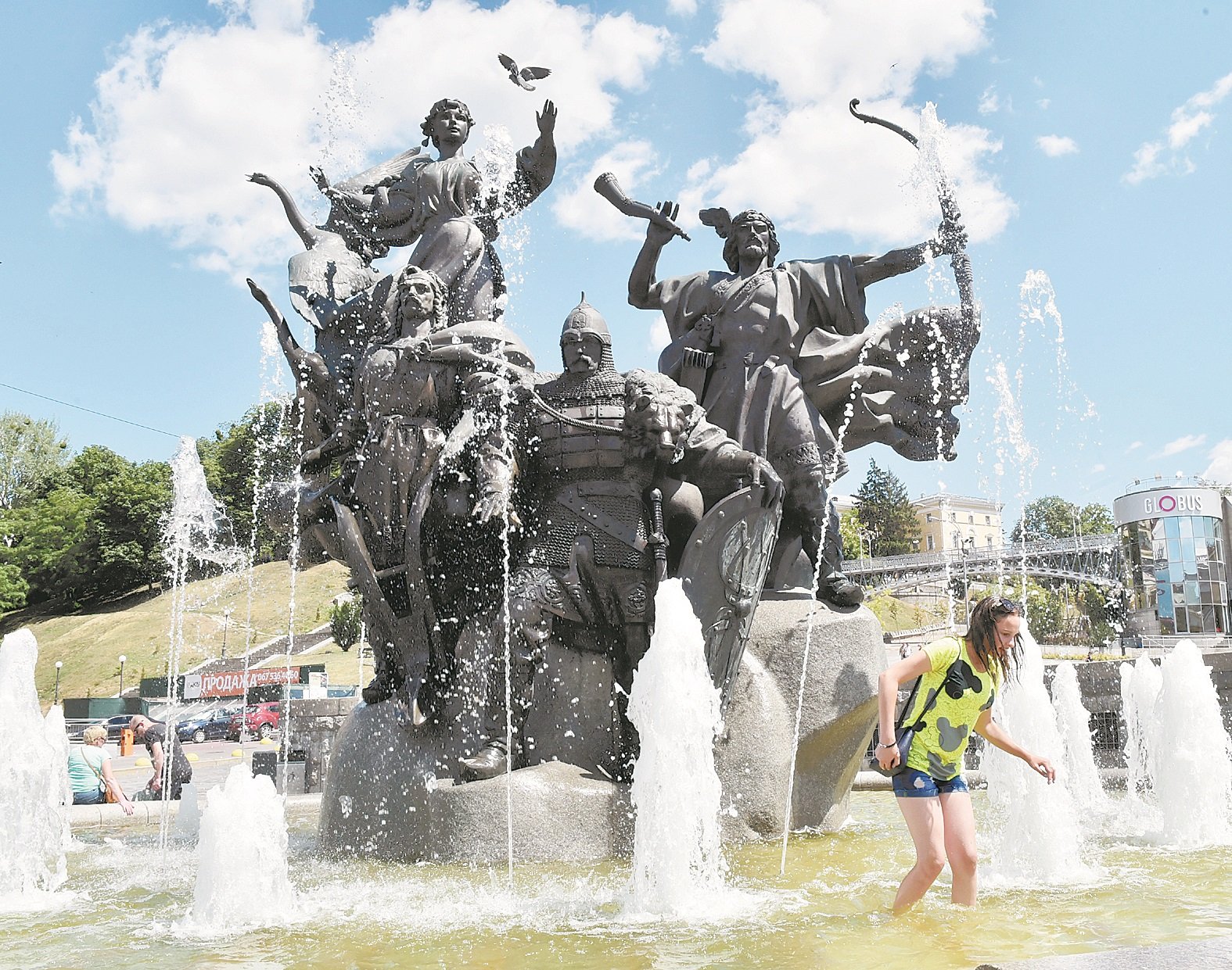 【乌克兰】基辅上空蓝天白云，气温却是热的让人难耐，一名女子走进雕像喷水池内淋水降温。