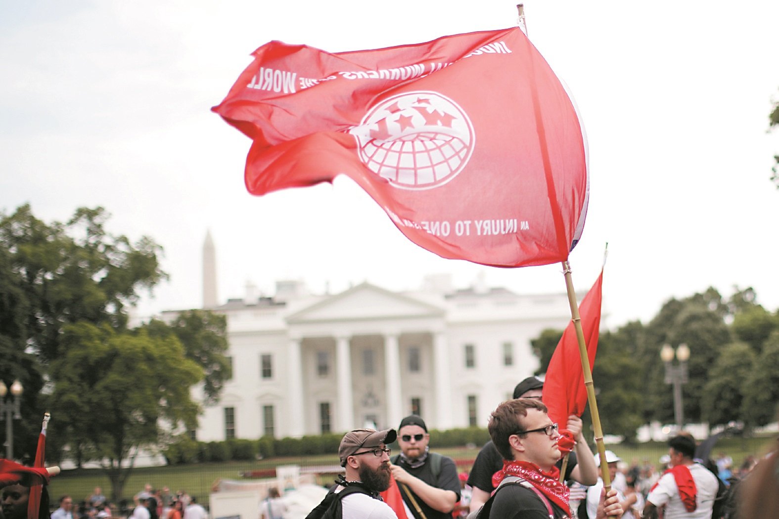 【美国】华盛顿的示威者，在白宫前的拉法叶公园集会，高举美国革命工会的旗帜，旗上写有“伤害一人就是伤害大家”的口号。