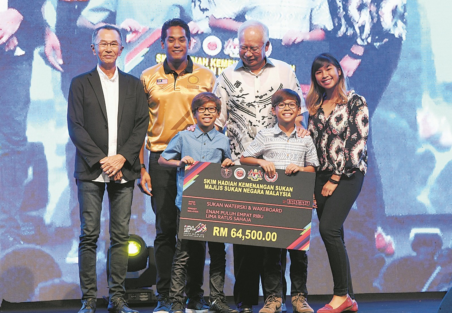 在本届吉隆坡东运贡献4金1银的熊氏滑水家族，获纳吉（站右2）大力表扬。左起为父亲熊英华、青体部长凯里、熊丽爱（右）、11岁的熊艾登（前排右）和9岁的熊亚当（前排左）。
