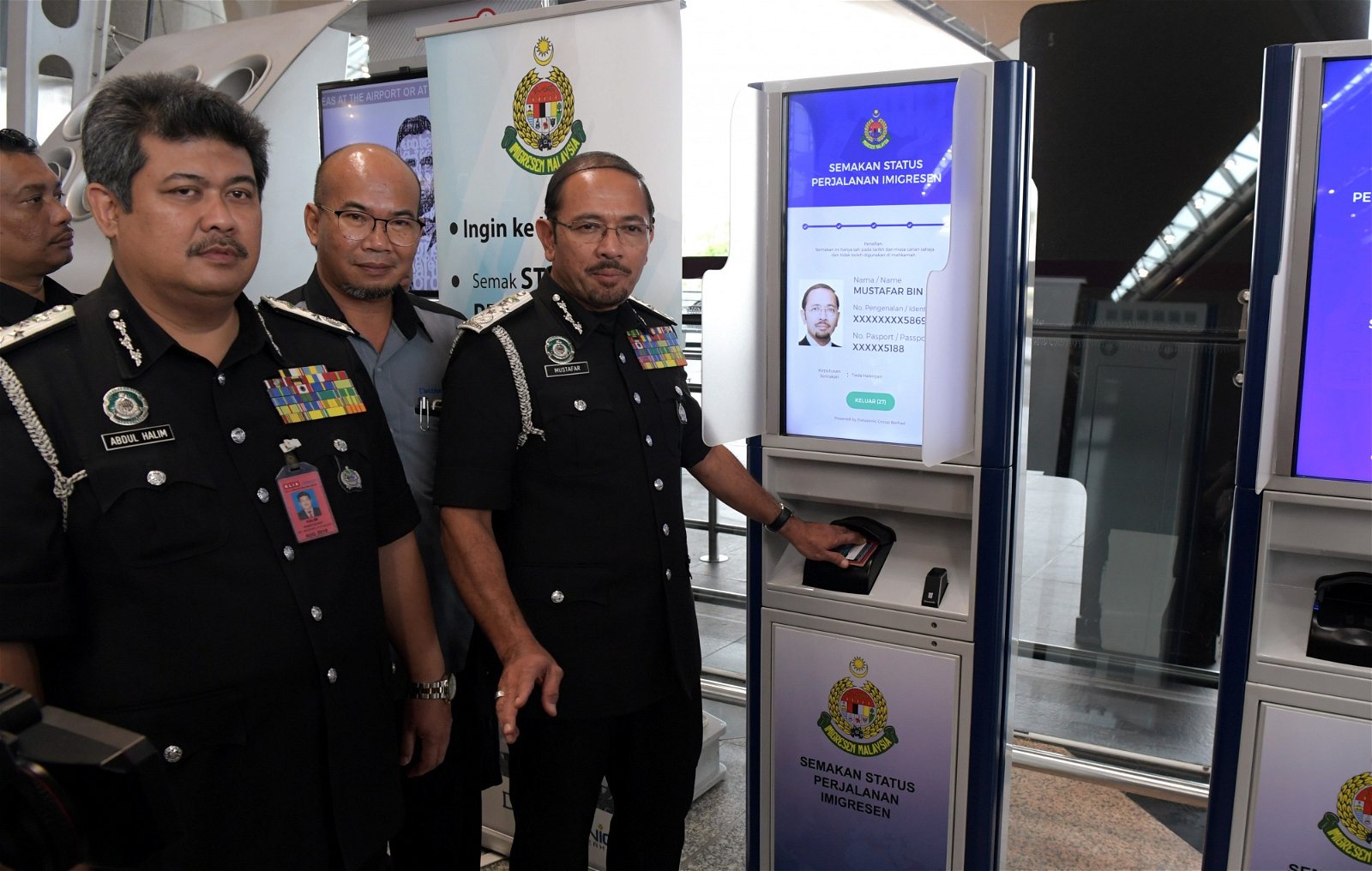 慕斯达法（右起）与一众官员向媒体示范，如何以国际护照在自动咨询机查询本身的通行许可状态。