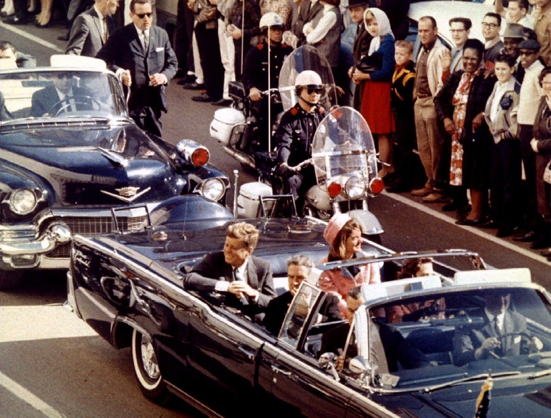 图为肯尼迪于1963年11月22日在得克萨斯州达拉斯市区乘坐敞篷车游行时，遇刺前的画面。