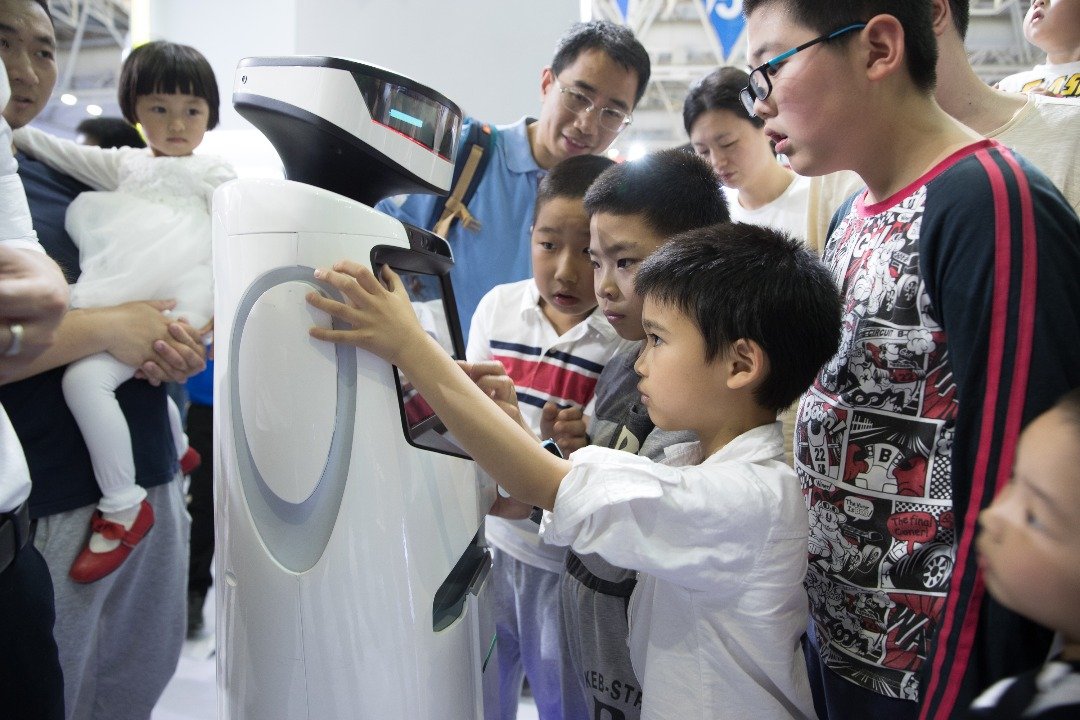 好奇的孩子们被一台设计精巧的机器人深深吸引，忍不著动手研究机器人身上的操控屏幕。