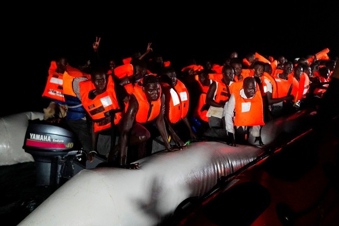 一群在救援行动中获救的难民，站在救援组织的橡皮艇上等候靠岸。