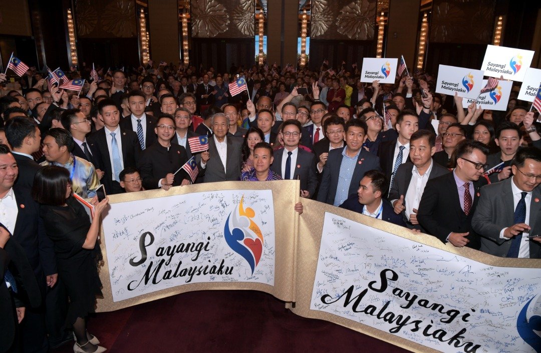 首相马哈迪（前排右8）与旅居中国的大马人会面晚宴上，出席者配合马来西亚国庆日到来，展示由旅华大马人签名的“爱马来西亚”横幅。