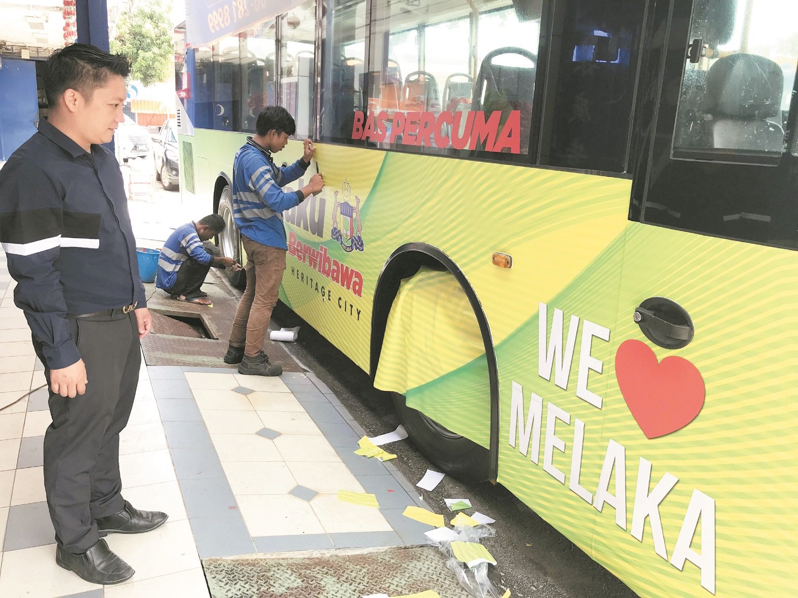 曾添兴监督员工为马六甲免费巴士贴上贴纸。