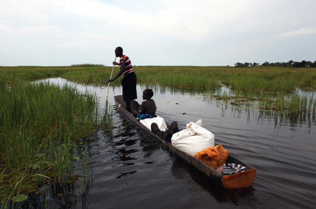 人们在领取救济品后，在长满芦苇的河上，用独木舟将食物载回家。这些粮食可协助他们，度过未来3个月的粮荒。