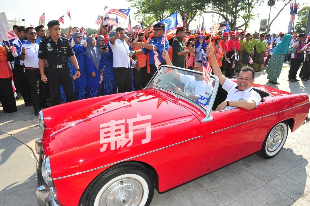 奥斯曼沙比安（右）乘坐吸睛的红色古董车入场，向夹道观看的民众挥手致意。（摄影：杨金森）
