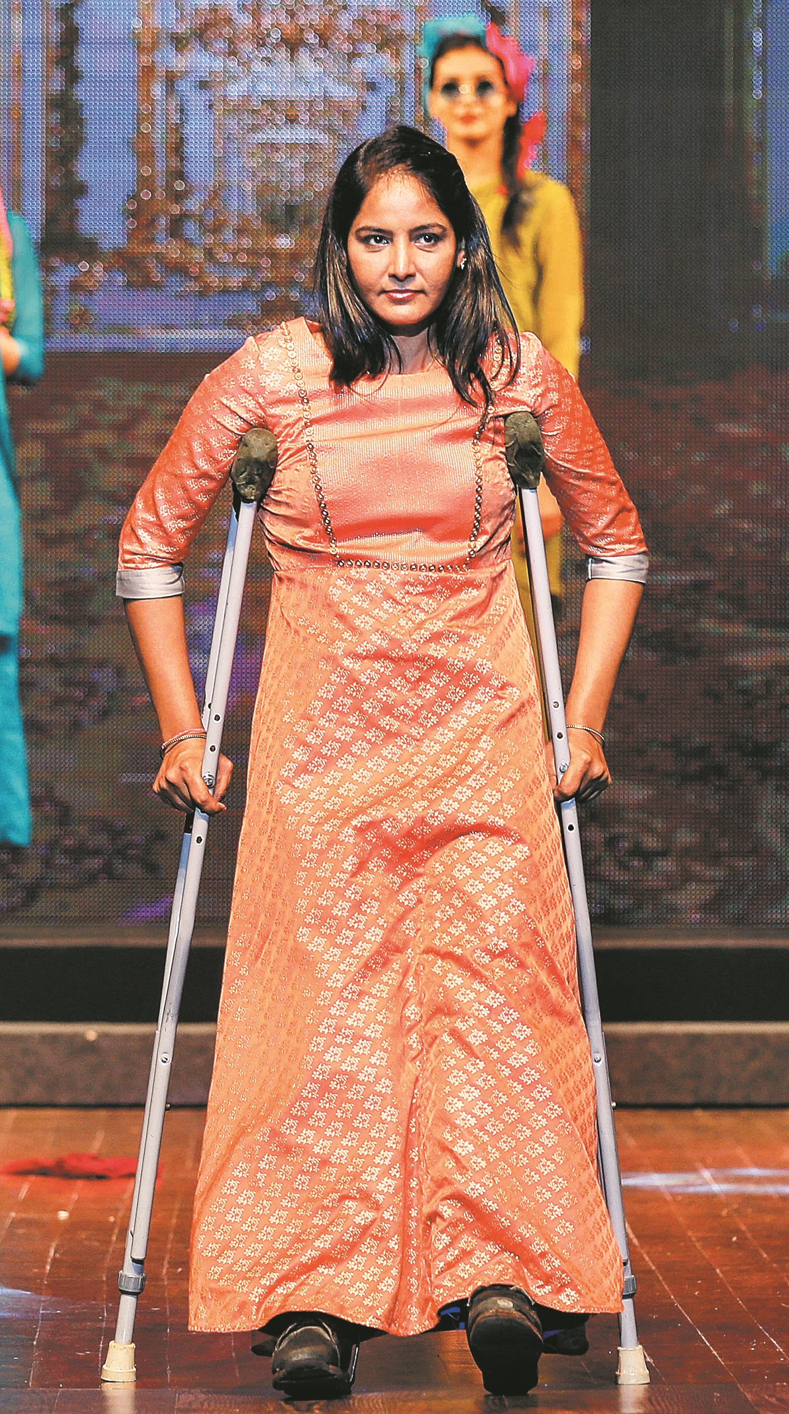 残疾模特儿带著腼腆笑意拄著枴杖，在时装秀伸展台上展现时装。