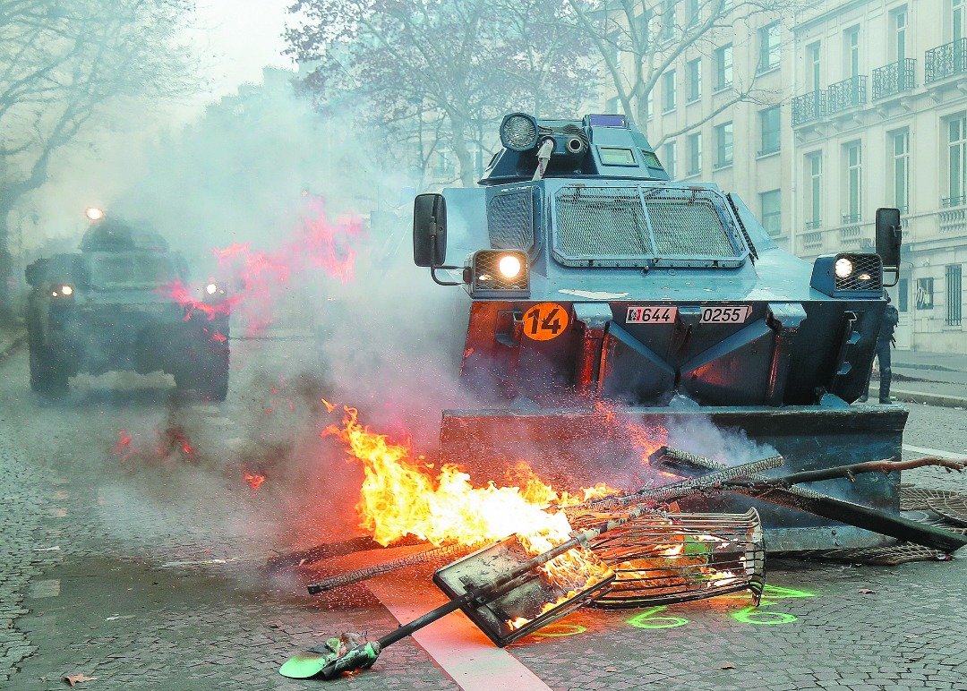 一辆辆由法国宪兵部队队员驾驶的装甲车缓缓地驶在香榭丽舍大道附近，途经一些由示威者制造的著火路障。