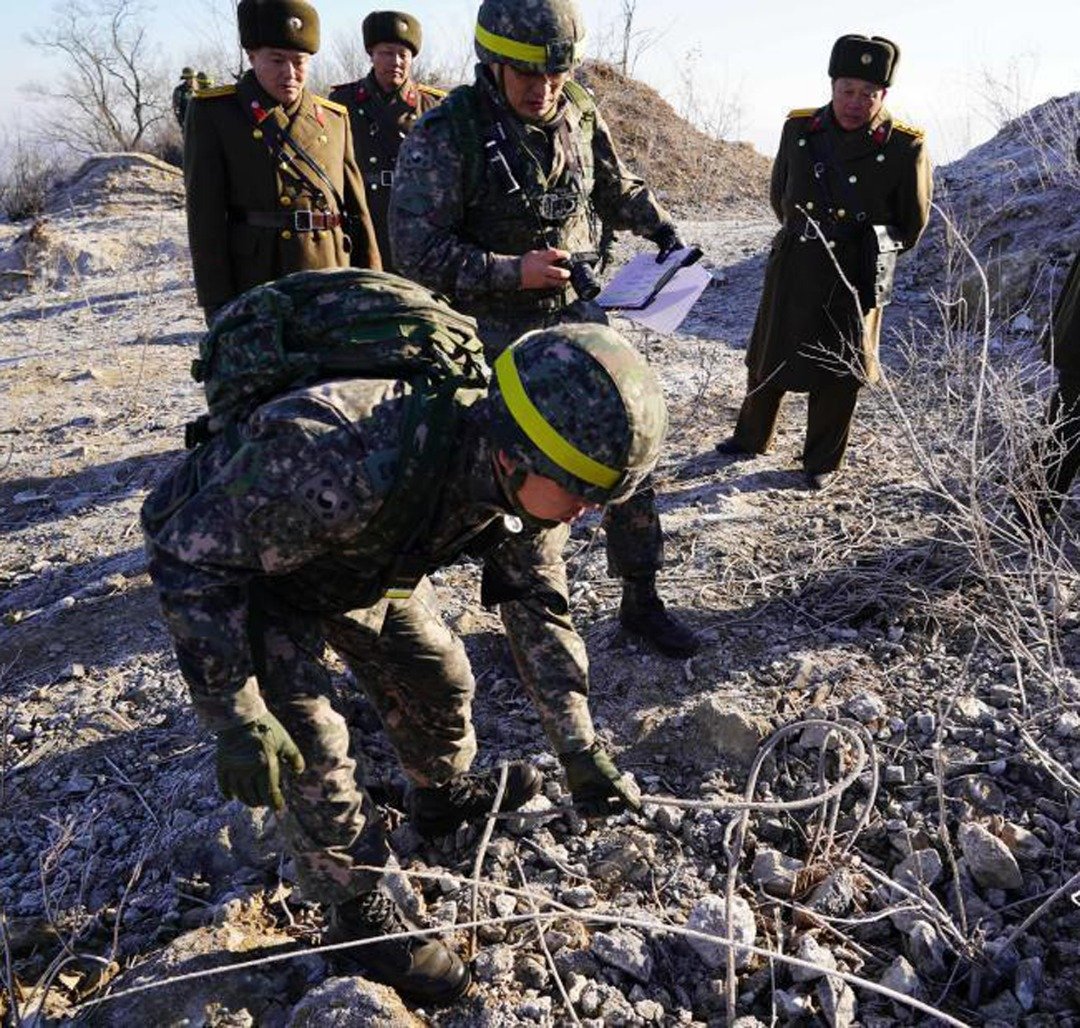 韩国的检验人员在3名朝鲜人员的陪同下，弯腰检查哨所被拆除后的情况，另一名韩方人员则在一旁做记录。据悉，双方均在友好的氛围中完成检验工作。