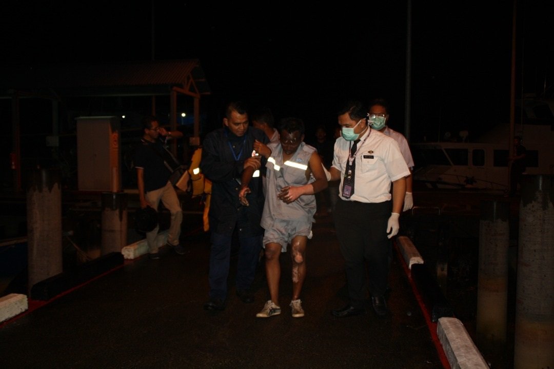 其中一名在爆炸意外中遭烫 伤的船员，在救援人员的搀 扶下离开意外现场。
