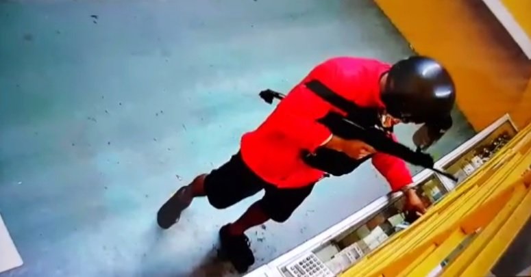 闭路电视画面显示，身穿红色风衣外套的匪徒手持冲锋枪，闯入手机店抢劫。