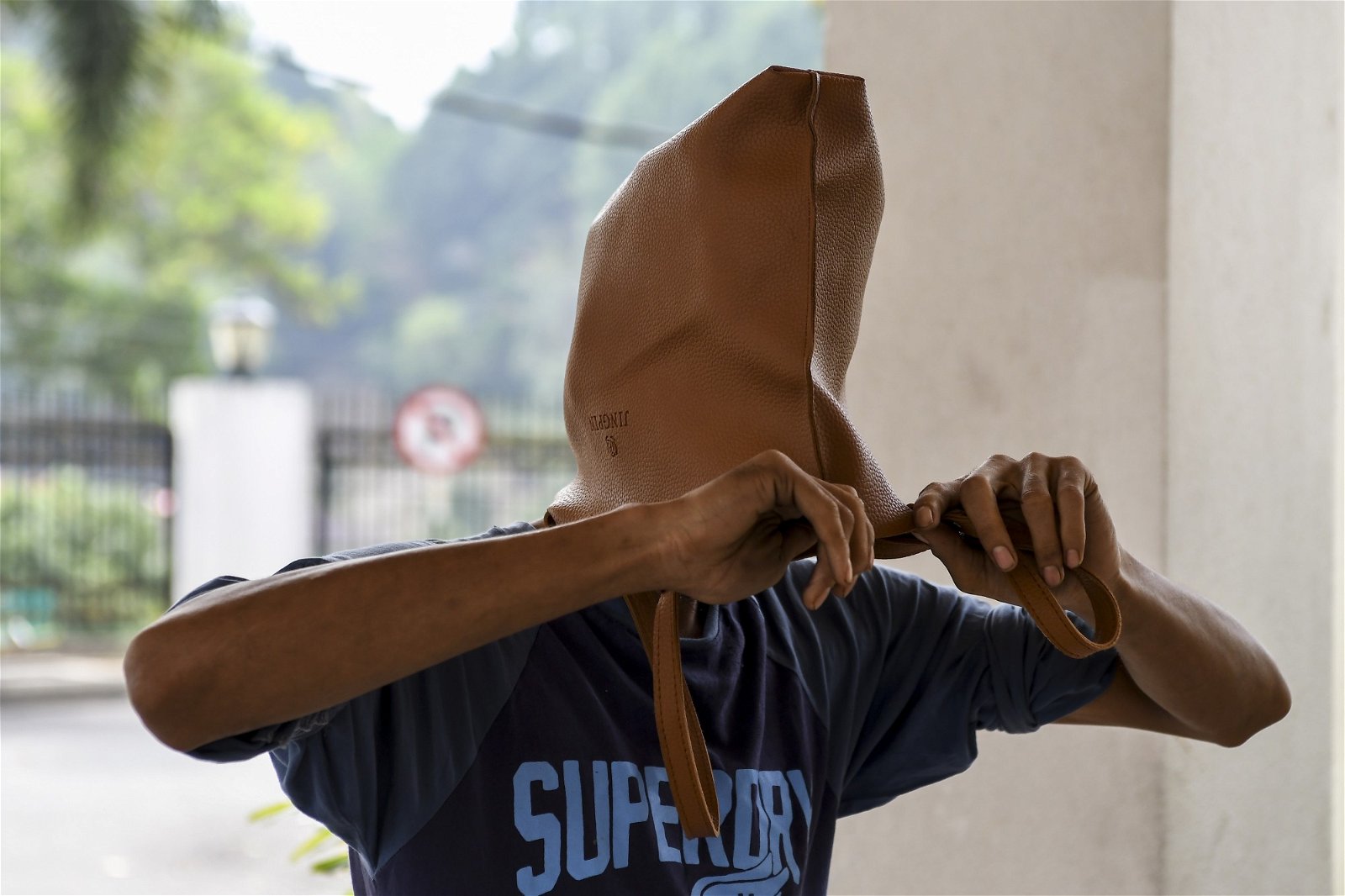 被告沙鲁以手提袋“套头”，避免被摄影记者拍到其面貌。