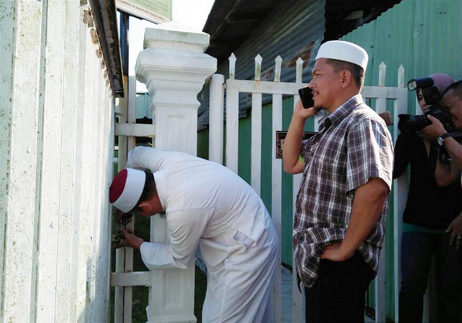 聂阿迪（右）吩咐墓场管理员将墓场大门锁上。