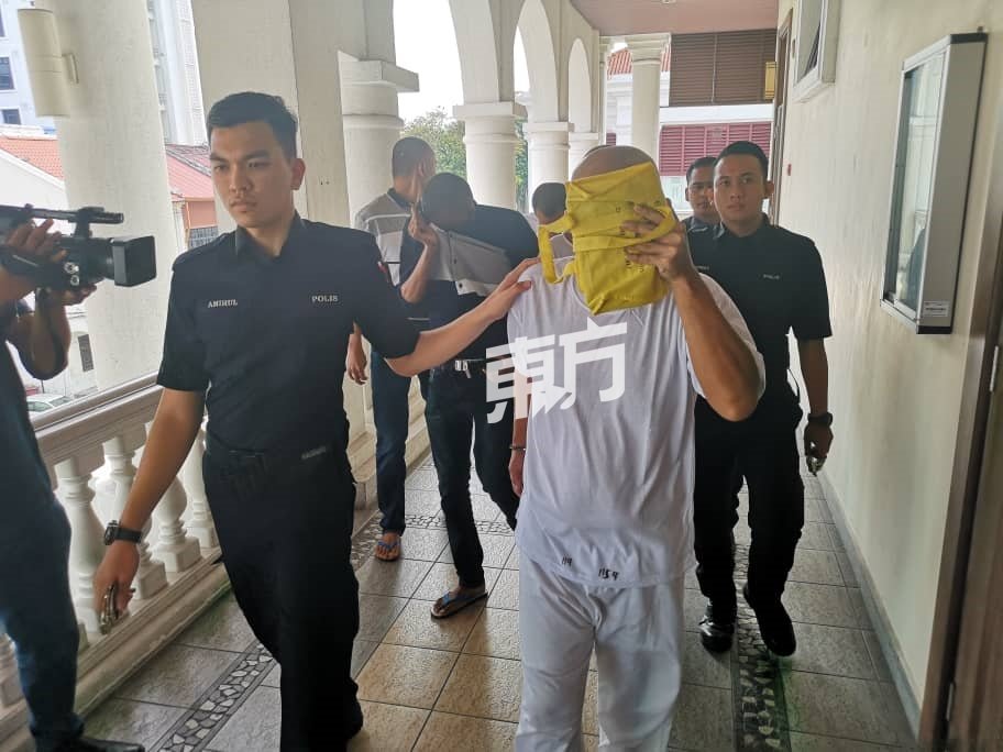 林振坤（右）被带上法庭时，以物品遮脸，避开媒体镜头。（摄影：吴维康）