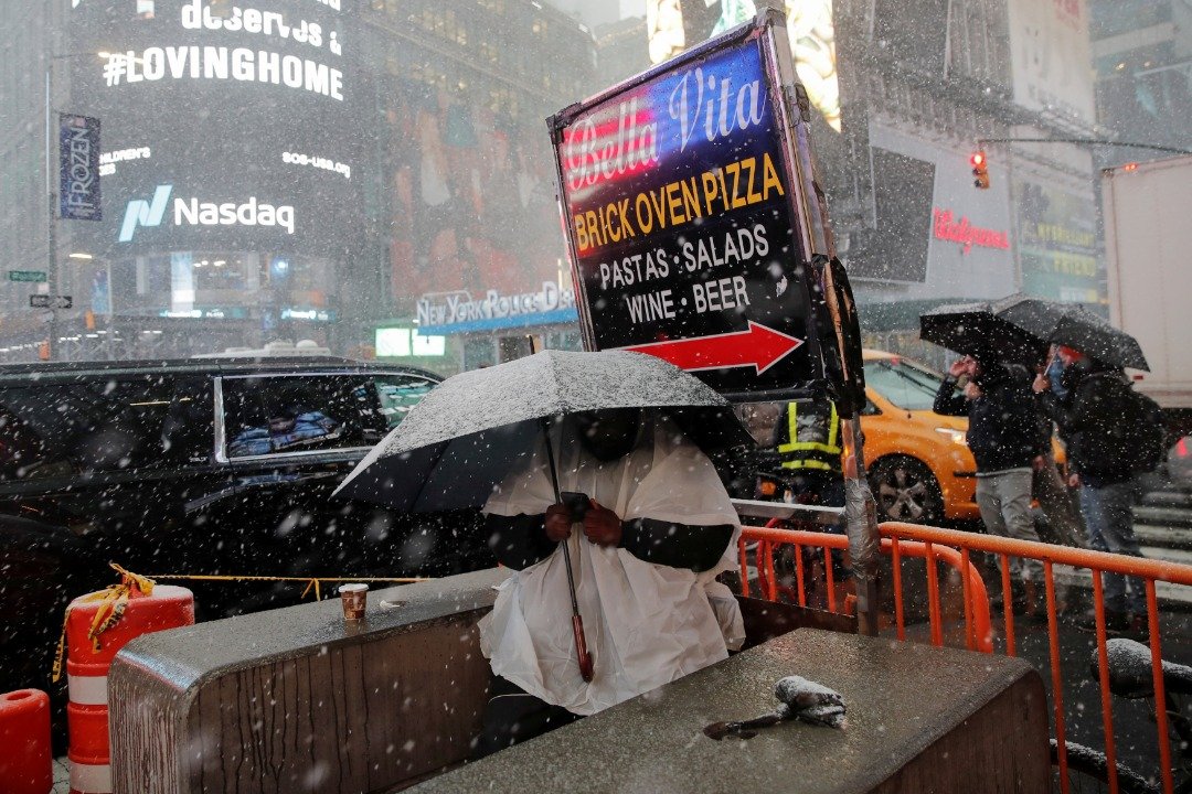 繁忙的纽约时报广场中，一名身穿御寒服饰的男子撑著一把大伞，试图将自己与冰冷的降雪隔绝开来。