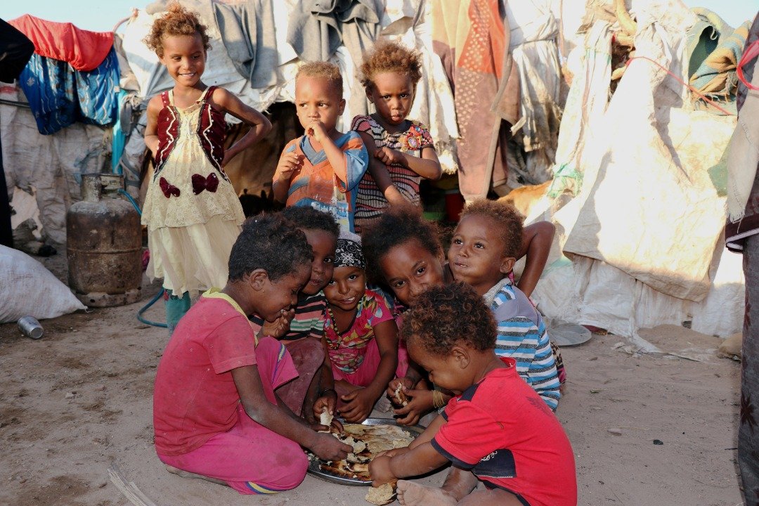 一群居住在亚丁市难民营的儿童，围著一盘面包，满足地享用著，有的还朝著镜头露出微笑。