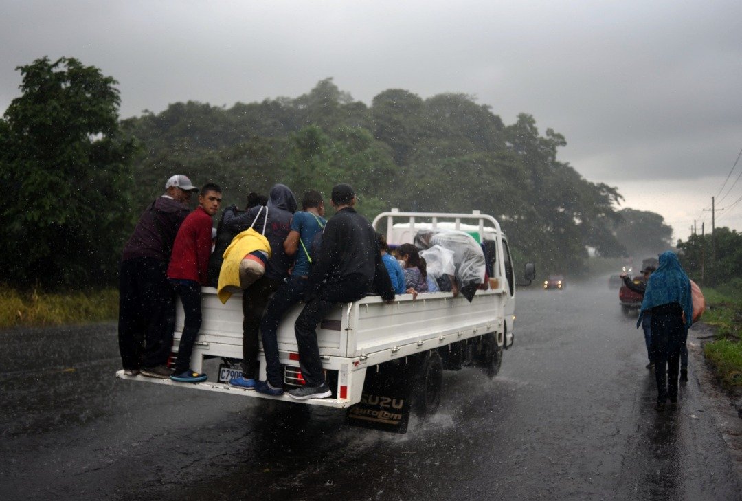 洪都拉斯的移民冒著滂沱大雨，坐在一辆白色卡车的后座；有些人甚至站在车尾，不顾犯险地朝著美国前进。