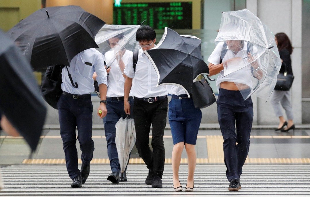 在东京街头，民众拼命的握紧手中的雨伞，以免被强风给吹走。