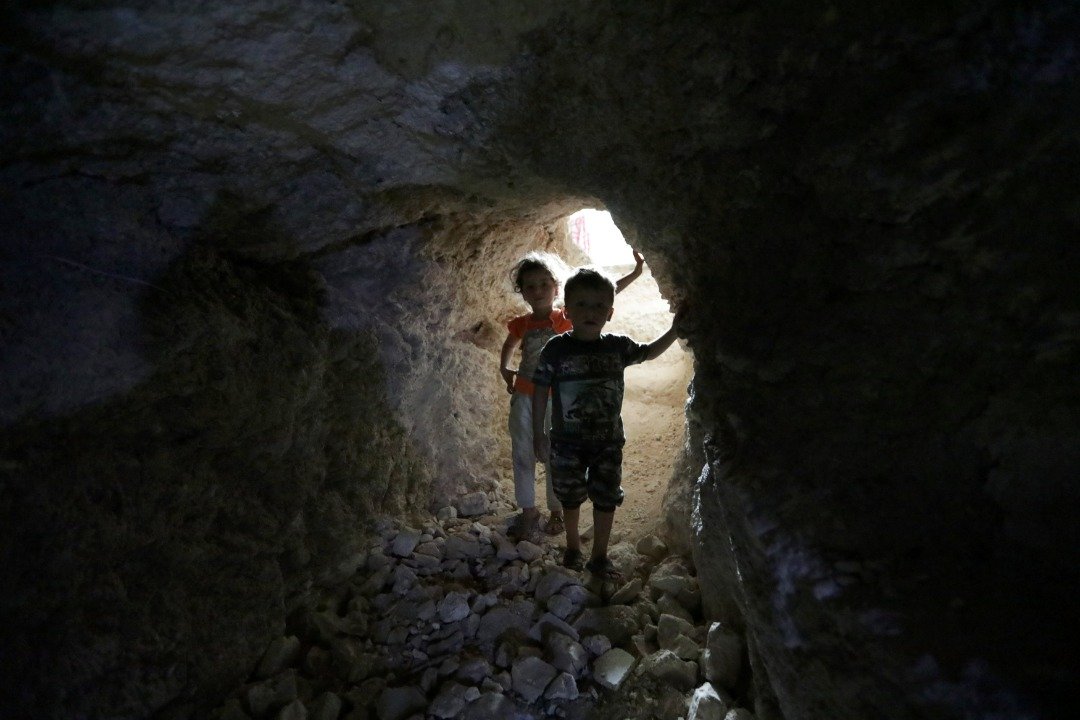 政府军对反抗军据点发起攻击前，伊德利卜省的平民挖掘地下洞穴，以便战乱来临时有个栖身之所。这是两个孩童进入伊德利卜省一个充当临时避难所的地下洞穴。