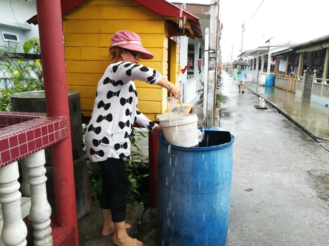 吉胆岛黄女士岛民趁下雨时，将之前储存的旧雨水倒掉，以便水桶可以盛过新的雨水。