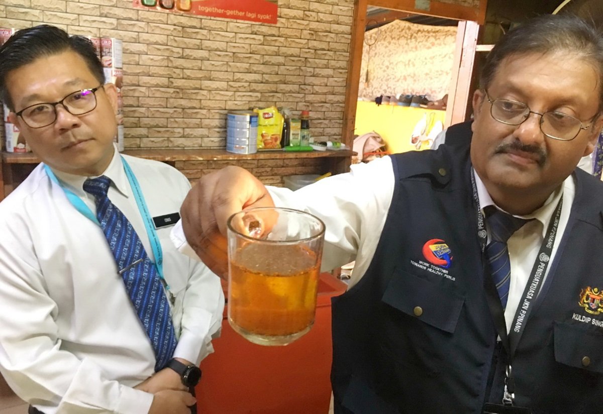 威南执法组主任库迪（右）展示渗入色素的茶，茶粉未溶，水已变色。旁为王勇元。