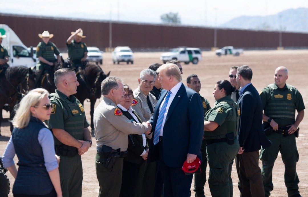 美国总统特朗普（中）到南加州边境城市卡莱克西科，视察新完工的边境栏栅，并与当地边防人员握手慰问。