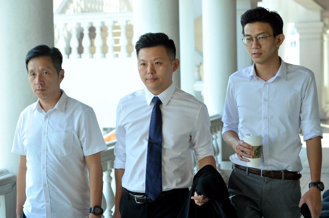 卢界燊（左2）在胡栋强（左起）及黄志毅的陪同下，以答辩人的身份出庭聆听审讯。