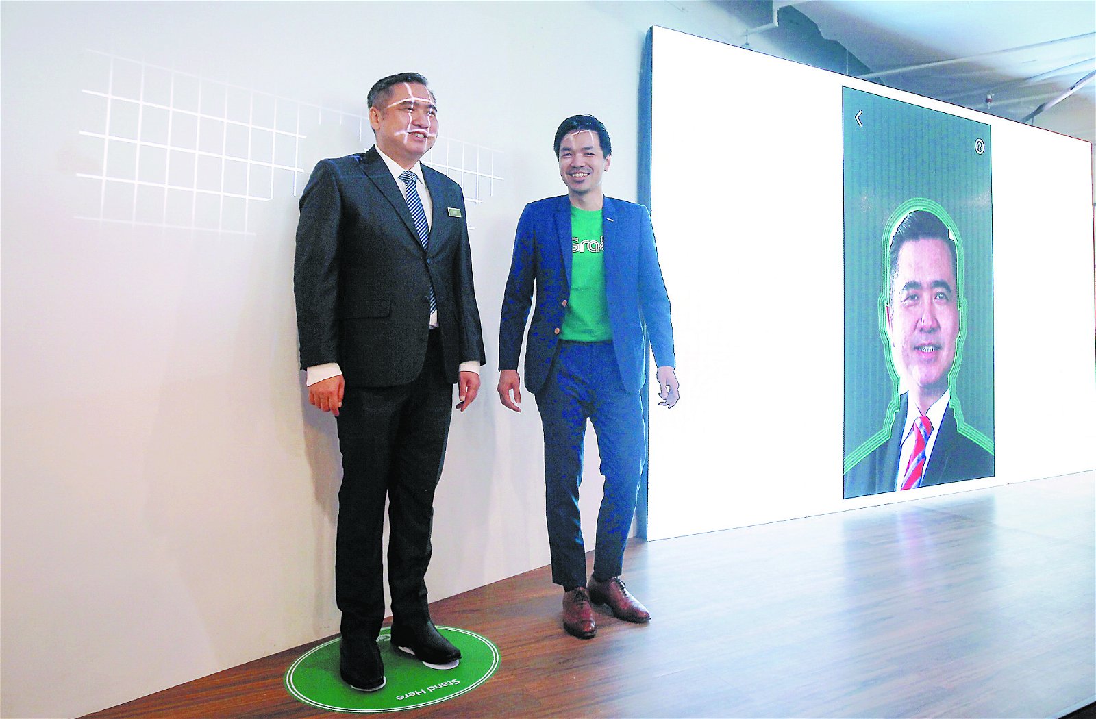 陆兆福（ 左） 边聆听吴士湘解 说，边体验脸部辨识模拟系统。
